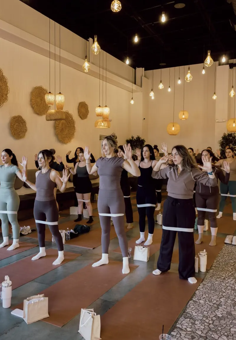 A group Pilates class standing on mats with resistance bands under warm pendant lights